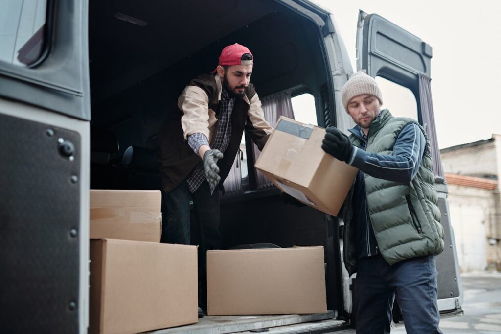 pexels-photo-4487512 Two delivery workers unload cardboard boxes from a van, showcasing teamwork and logistics.